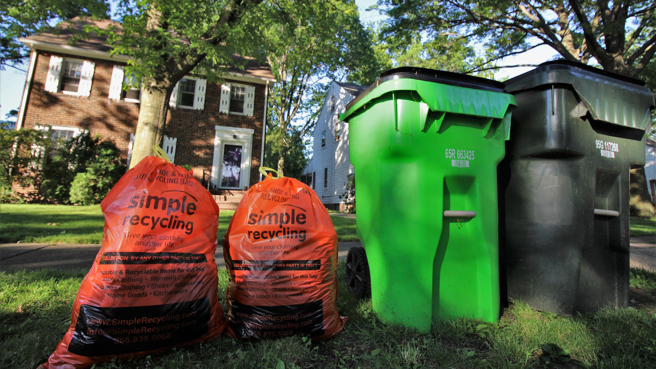 Two orange Simple Recycling bags to the left of a green recycling bin