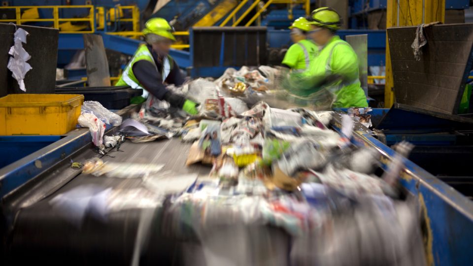 Workers separating paper and plastic on a conveyor belt in a recycling facility